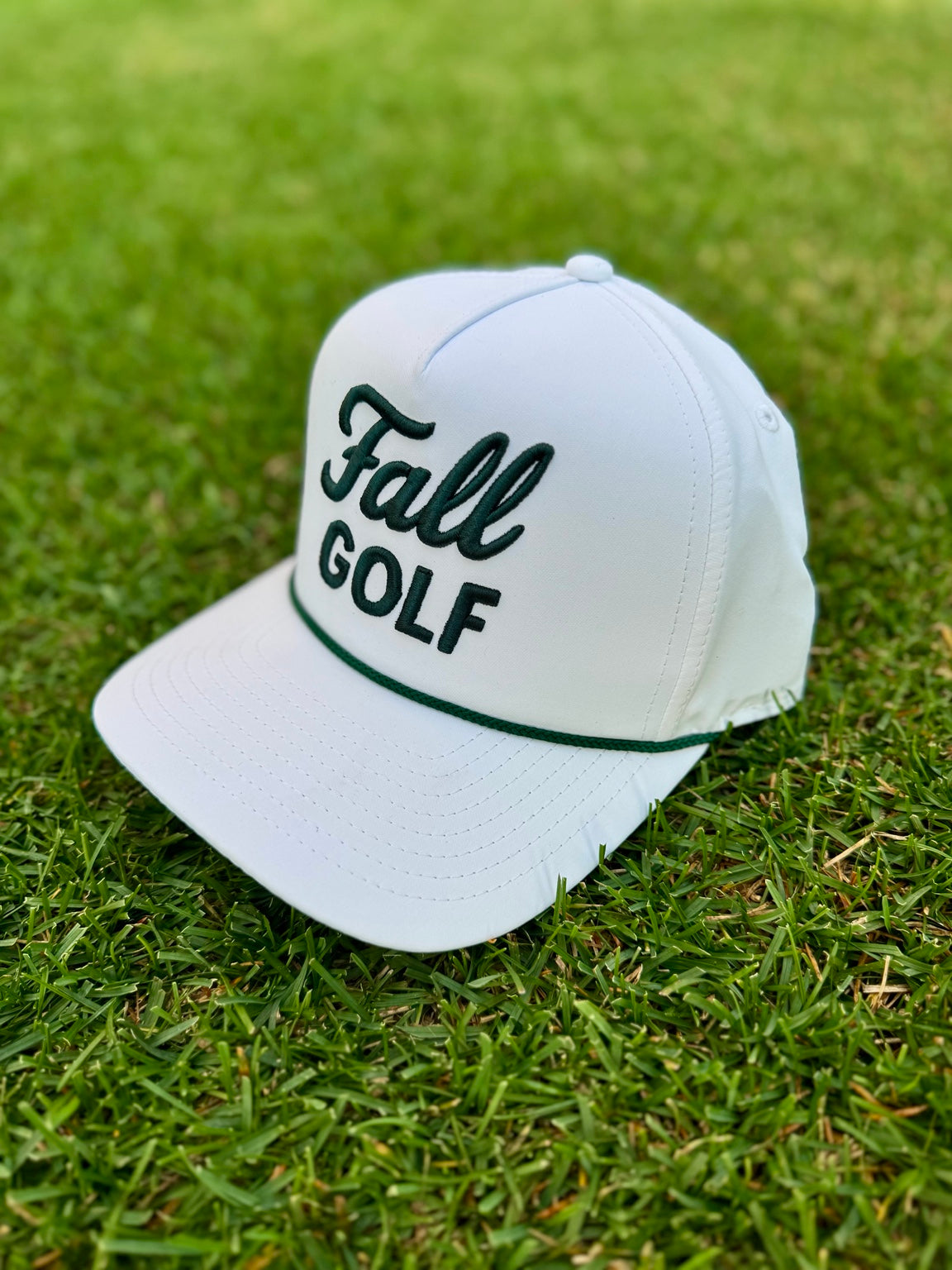 White Fall Golf rope hat with dark green embroidery resting on the grass.